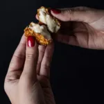Manos con uñas pintadas abriendo una croqueta.