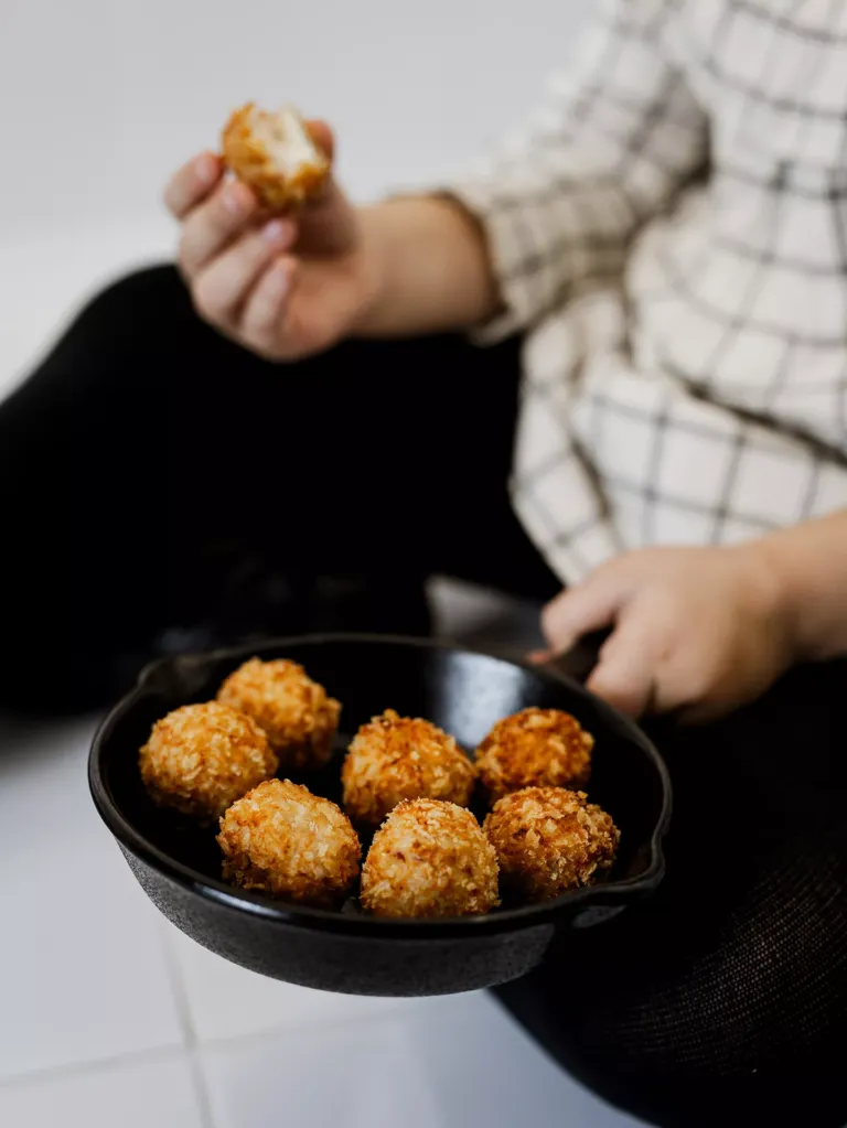 Niña sosteniendo una sartén de croquetas y una croqueta.