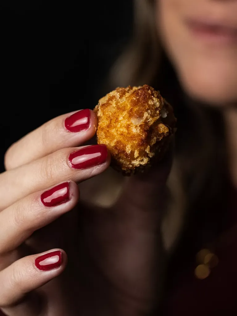 Mujer con uñas pintadas sosteniendo una croqueta.