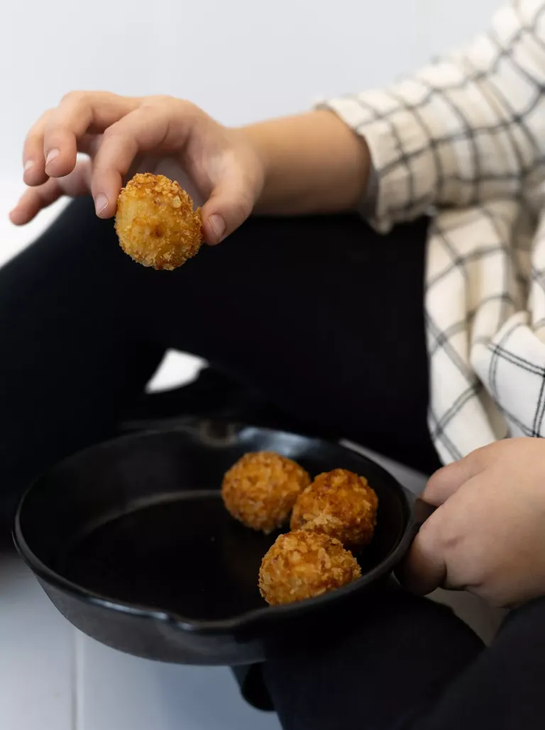 Persona con una croqueta en mano y otras en sartén.